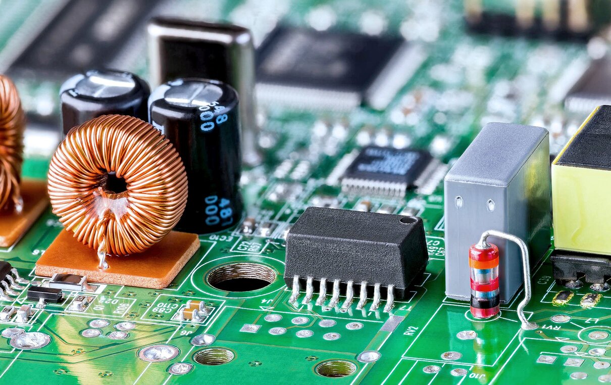 Coil or varied electronic components on green printed circuit board detail. Orange inductor with copper wire, black ethernet isolation transformer and diode or electrolytic capacitors on PCB with SMD.