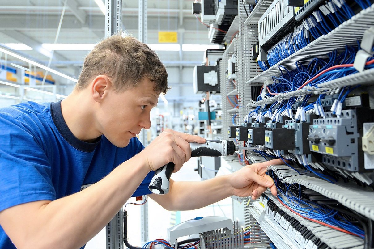 young operator assembles machine in a modern high tech factory - production of switch cabinets for industrial plant