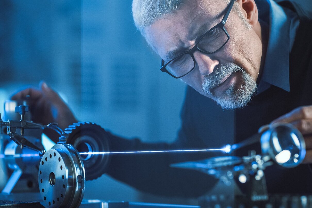 Close-up Portrait of Focused Middle Aged Engineer in Glasses Working with High Precision Laser Equipment, Using Lenses and Testing Optics for Accuracy Required Electronics